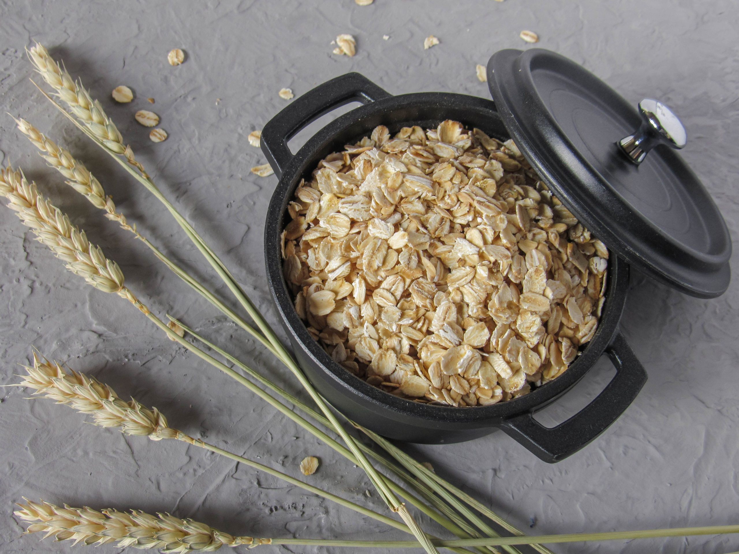 Our Products Flat lay of rolled oats in a black pot surrounded by wheat stalks on a textured surface.