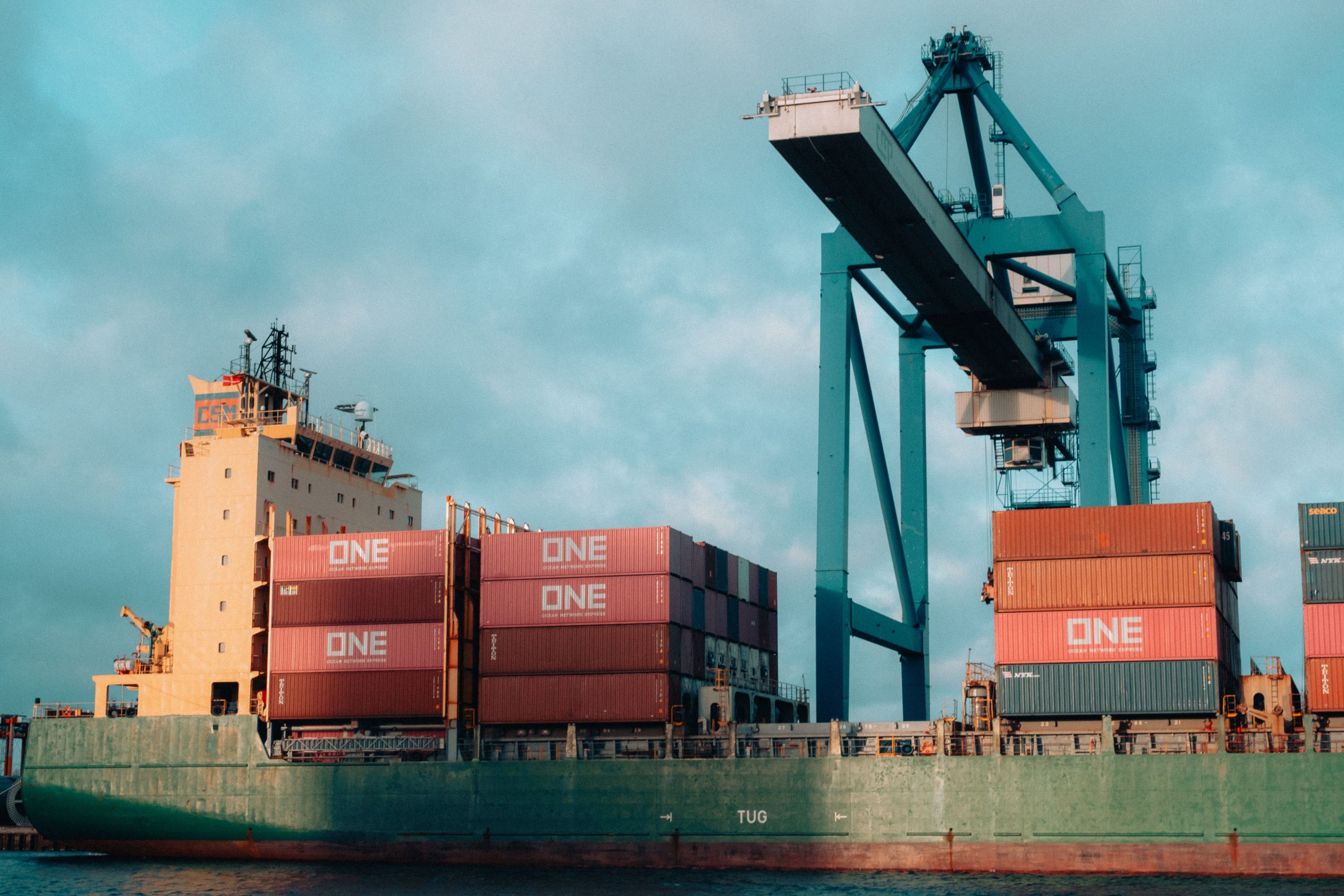 Our Products Large cargo ship loaded with colorful containers at a bustling industrial port.